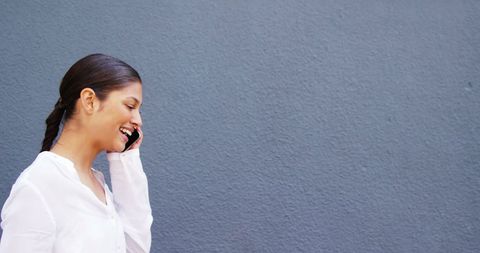 Cheerful Latina Woman Talking on Phone Against Blue Wall