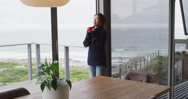 Happy asian woman drinking coffee and thinking at window alone. Spending quality time at home.