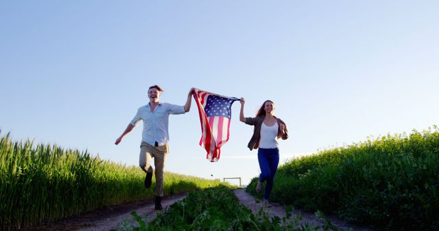 A young Caucasian man and woman are joyfully running through a field holding an American flag, with copy space. Their cheerful expressions and the flag symbolize patriotism and freedom.
