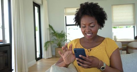 African american woman checking smartphone on couch in modern minimalist living room