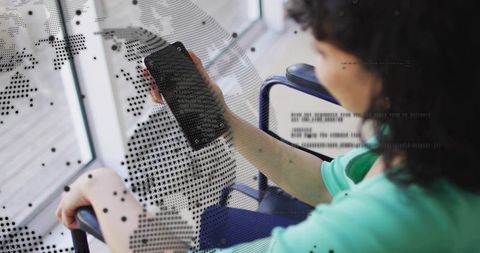 Wheelchair user holding smartphone by window with dotted world map overlay, accessibility