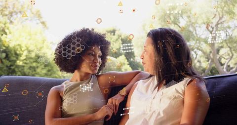 Two women sharing relaxed conversation on outdoor couch with augmented reality overlay