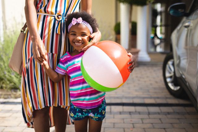 Portrait of happy african american girl with ball holding african american mid adult mother's hand. unaltered, family, lifestyle, childhood, leisure activity and weekend activity.