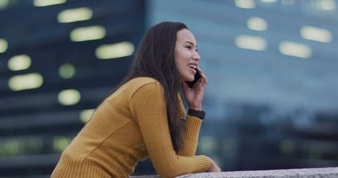 Young woman leaning on railing talking on phone at twilight on urban office terrace
