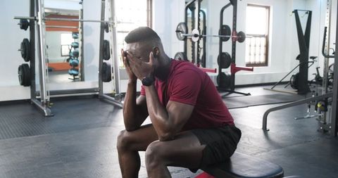 Frustrated gym goer sitting on bench with face in hands