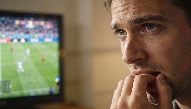 Nervous sports fan biting fingernails while watching tense soccer match on flat-screen tv