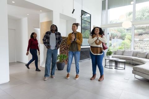 African american friends entering modern open-plan living room applauding new home tour