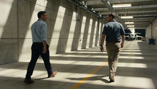 Two technicians walking toward private jet in sunlit hangar along yellow centerline