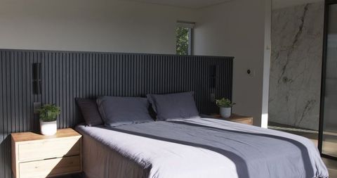 Sunlit modern bedroom featuring king bed, slatted headboard, marble ensuite and greenery