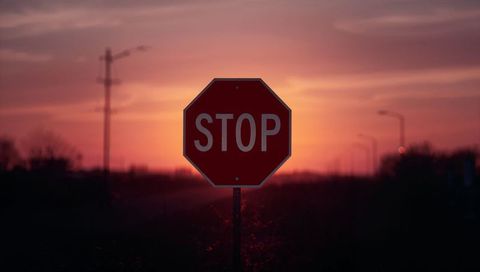 Glowing stop sign silhouetting against dramatic orange sunset along quiet roadside