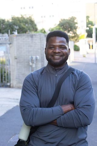 Confident african man standing with arms crossed smiling outdoors carrying foam roller