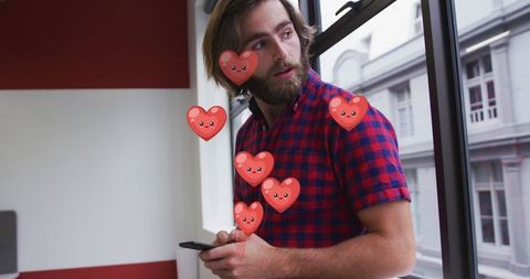 Bearded Man with Smartphone Surrounded by Animated Hearts at Office Window