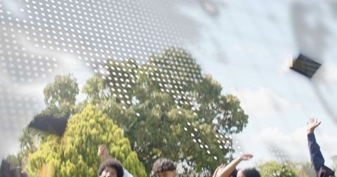 Graduates tossing mortarboards into air on sunny campus with dotted graphic overlay