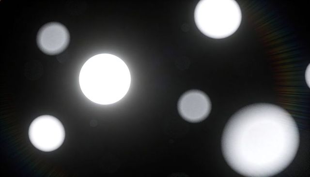 Luminous bokeh orbs floating on deep black field with halo lens flare effect