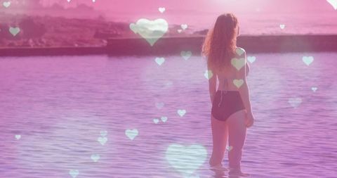 Woman Standing in Shallow Water at Sunset with Heart Bokeh and Dreamy Pink Glow