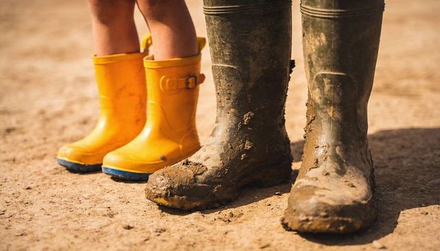 Parent and child standing in muddy wellington boots beside bright yellow rain boots closeup