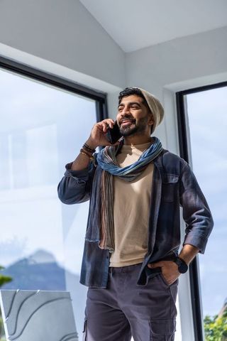 Remote worker talking on smartphone by sunlit panoramic windows in modern loft office