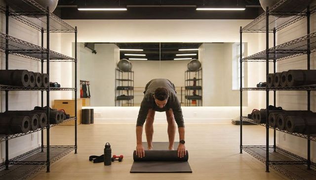 Male rolling foam roller on mat in minimalist gym preparing mobility and recovery routine