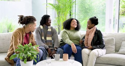 Diverse friends chatting on light sofa, sipping coffee in bright modern living room
