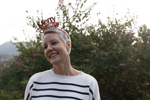 Senior woman smiling outdoors wearing merry christmas headband during golden hour
