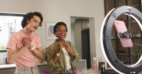 Clapping and Singing Hosts Filming Cooking Vlog with Ring Light in Modern Kitchen