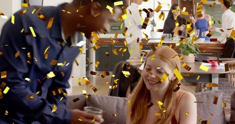 Red-haired woman smiling on sofa amid gold confetti during lively home kitchen celebration