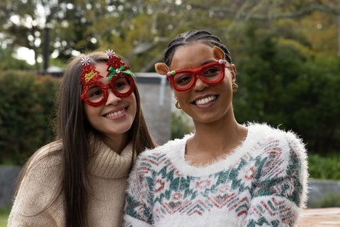 Smiling multicultural women wearing festive novelty glasses and cozy sweaters outdoors