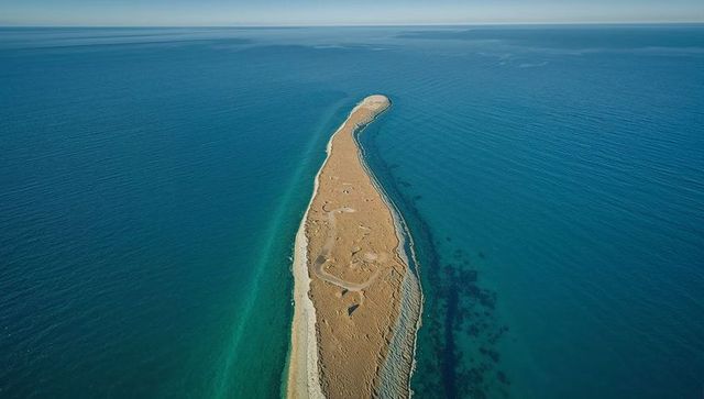 Aerial view of narrow sandbar curving into turquoise horizon with shallow tidal pools