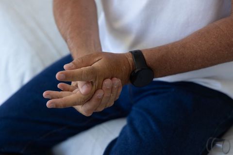 Mature african american man rubbing hand on sofa wearing smartwatch showing wrist discomfort