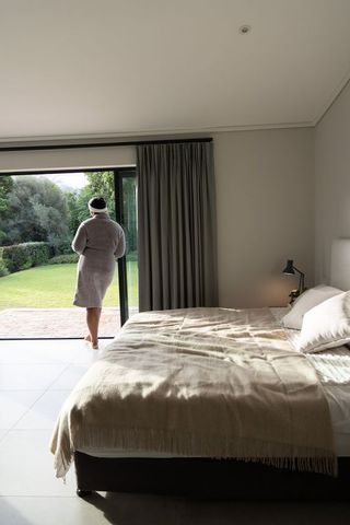 Woman standing barefoot at sliding glass door in bathrobe overlooking sunlit garden