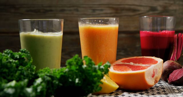 Three glasses of colorful fresh juices on a wooden table, surrounded by various fruits and vegetables. Ideal for promoting a healthy lifestyle, nutrition and wellness concepts, or menus for juice bars and cafes.