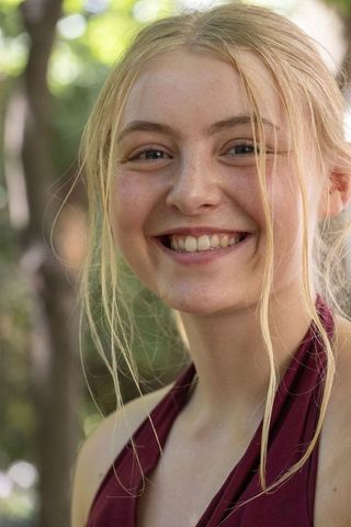 Sunlit smiling young woman with freckles and loose hair strands wearing maroon halter top