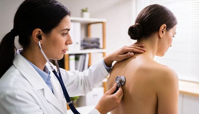 Female doctor listening to patient lung sounds during back examination in clinic