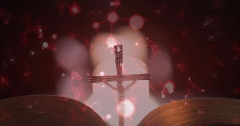 Metal crucifix silhouette over open bible with candlelight bokeh and warm amber halo for devotional