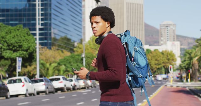 Young man with backpack walking on urban street, looking at surroundings, and holding mobile phone. Ideal for illustrating themes of travel, adventure, urban exploration, young adult lifestyle, and solo journeys. Useful for travel blogs, tourism promotions, city guides, and lifestyle articles.