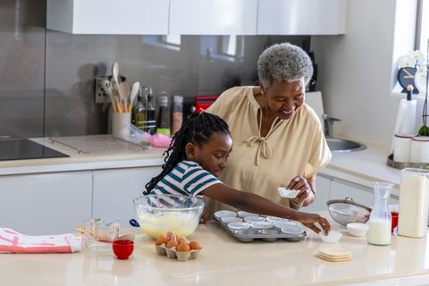 African american grandmother guiding granddaughter baking cupcakes together in kitchen