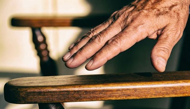 Hovering elderly hand above wooden armrest, close-up of veins, wrinkles and texture