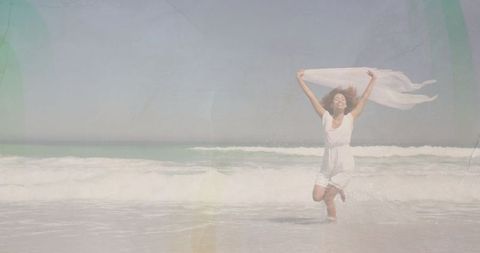 Carefree woman with sheer scarf running along shoreline