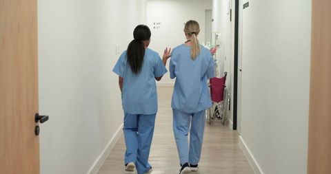 Two nurses walking down clinic hallway discussing patient care next to pink wheelchair