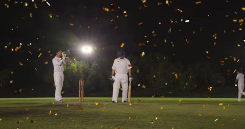 Batsman standing at crease celebrating under floodlights with golden confetti falling
