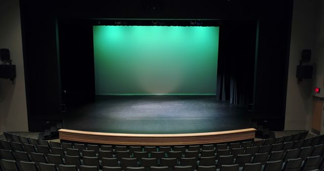Depicts an empty theater with green stage lighting and rows of seats in the foreground. Could be used for themes of performance, art, theater productions or to promote events and venues.
