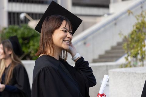 Smiling diverse female graduate adjusting hair holding diploma with red ribbon on stairs