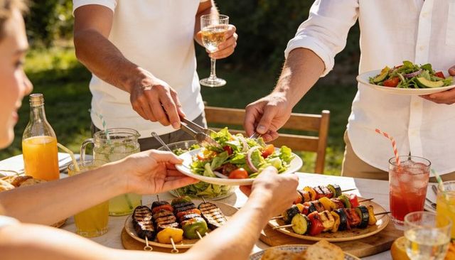 Friends sharing fresh salad and grilled vegetable skewers during outdoor summer lunch