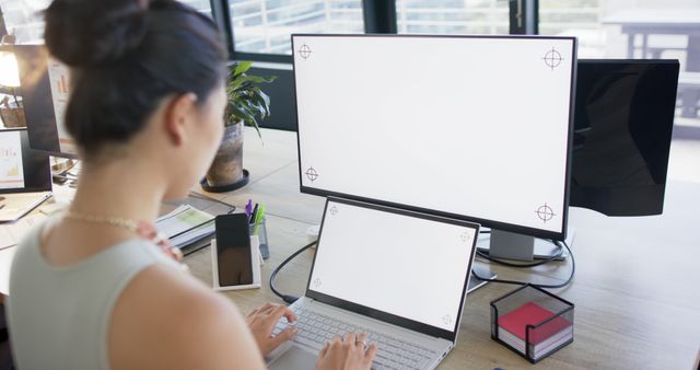 Woman working on a laptop with dual monitors in a modern office, showcasing productivity and technology integration. Ideal for illustrations on modern workspaces, professional environments, and tech-assisted working style.