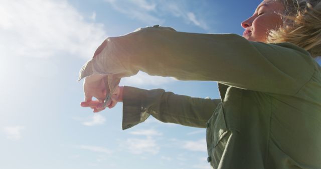 Woman stretching arms outdoors wearing green jacket. Suitable for use in lifestyle, fitness, and health-related topics. Ideal for promotions of outdoor activities, mental health awareness, and healthy living campaigns.