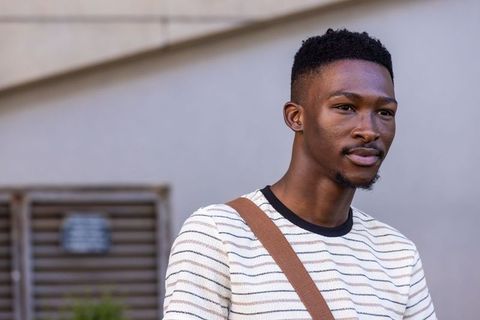 Young african man wearing striped sweater and brown crossbody bag looking confident on urban street