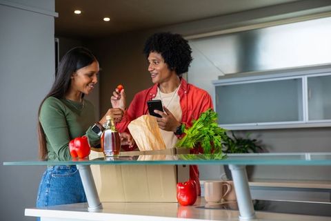 Diverse Couple Unpacking Groceries with Smartphone in Kitchen