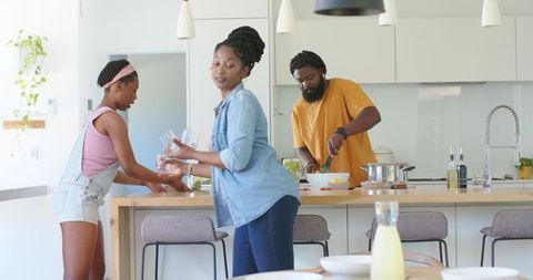 African american family cooking together in sunlit modern kitchen at wooden island