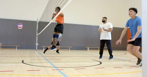 Diverse male volleyball team practicing dynamic net block with coach guiding