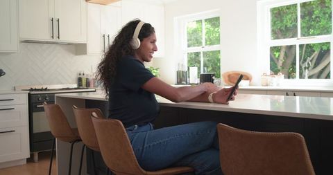 African american woman listening with headphones while using smartphone at kitchen island